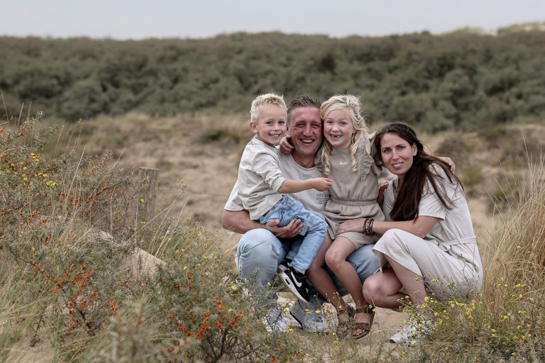 Portret Een gezin bestaat uit twee volwassenen en twee kinderen, zittend in een groene, zandige omgeving.